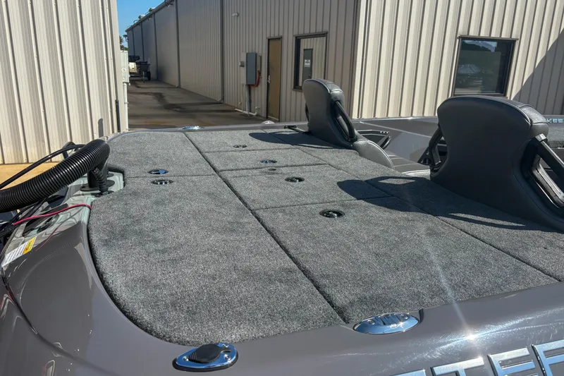 Slide: The Image of 2026 Skeeter ZXR 19 boat deck with gray carpet and seating, parked near industrial buildings. - 5