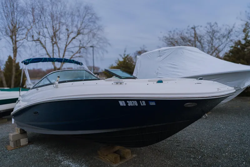 Slide: The Image of 2013 Sea Ray 220 Sundeck boat on land, covered, with trees in the background. - 1
