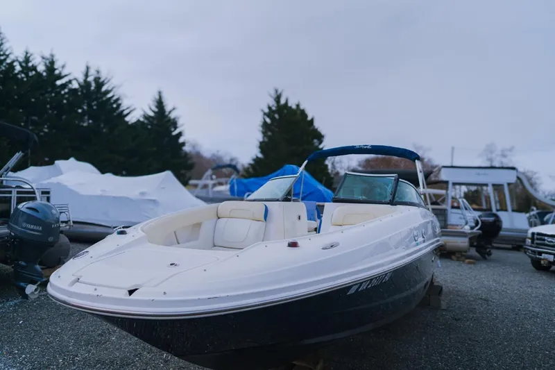 Slide: The Image of 2013 Sea Ray 240 Sundancer boat on gravel lot, surrounded by trees and other boats. - 1