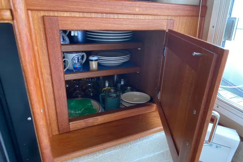 Slide: The Image of Wooden cabinet with dishes and mugs inside, located on a 2003 American Tug 34 boat. - 35
