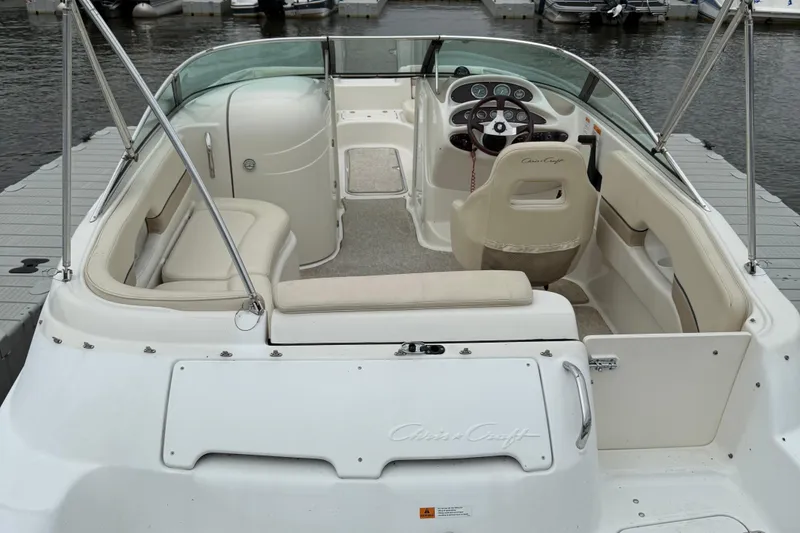 Slide: The Image of 2000 Chris-Craft 230 Deck Boat interior, featuring helm and seating, docked by the water. - 3