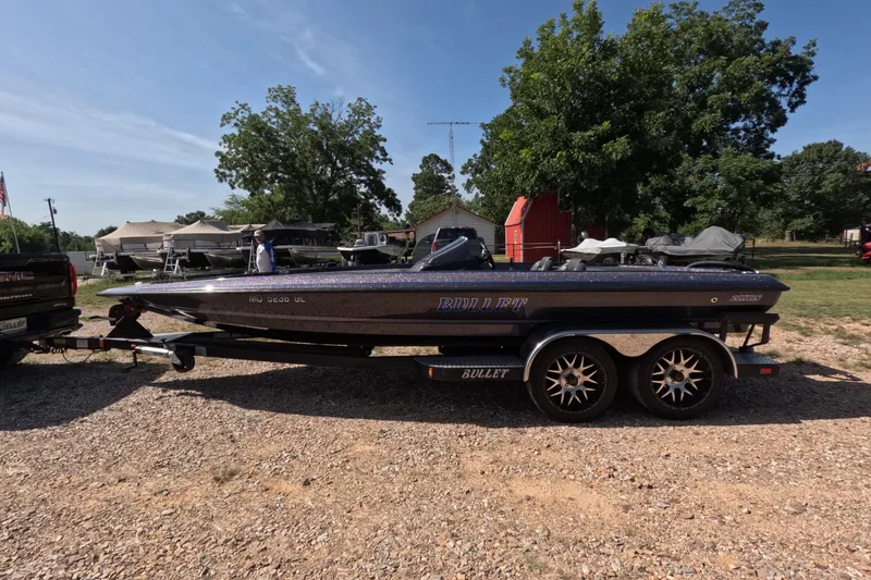 Slide: The Image of 2021 Bullet 21XRS boat on trailer, parked outdoors with trees and buildings in the background. - 1