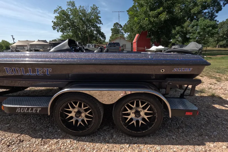 Slide: The Image of 2021 Bullet 21XRS boat on trailer, parked outdoors with trees and buildings in background. - 9