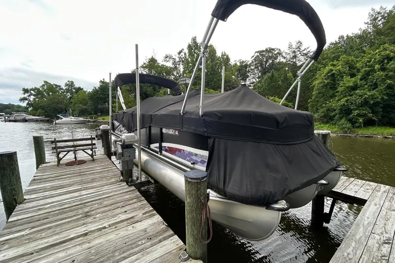 Slide: The Image of 2010 Premier 250 S-Series pontoon boat docked with black cover, surrounded by lush greenery. - 26
