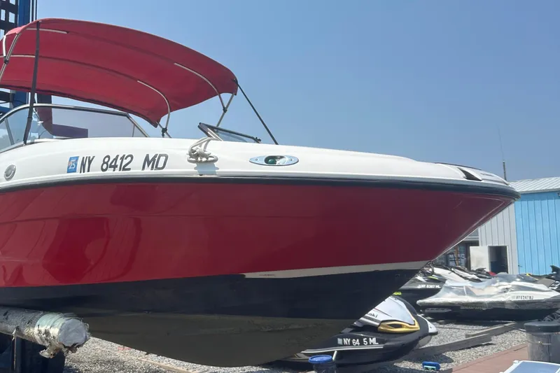 The Image of 2007 Yamaha Boats SX210 with red hull and canopy, docked under clear blue sky. - 0