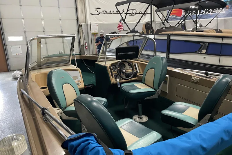 Slide: The Image of 1997 Lund 1700 Pro Sport boat interior with green and beige seating in a showroom. - 7