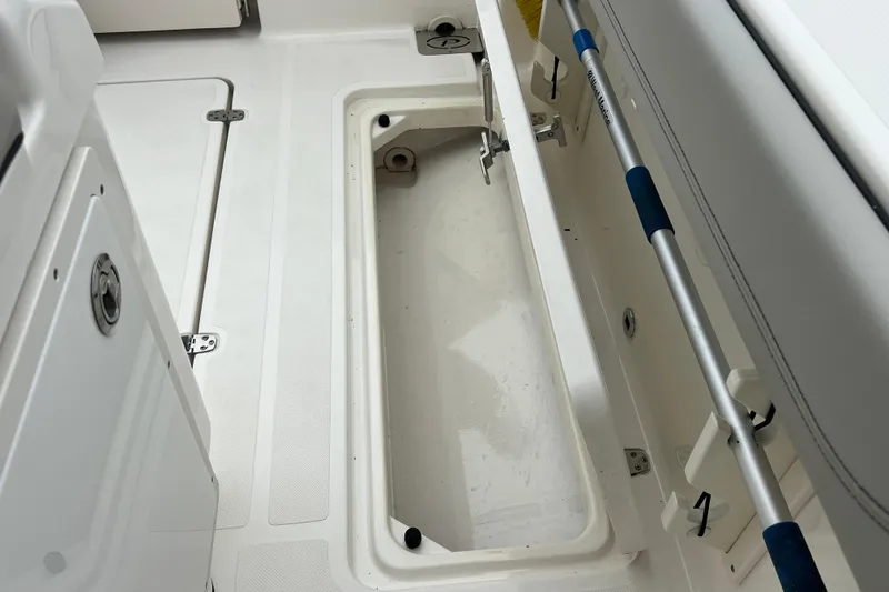 Slide: The Image of 2023 Pursuit S 268 Sport boat storage compartment with open hatch and cleaning brush. - 26
