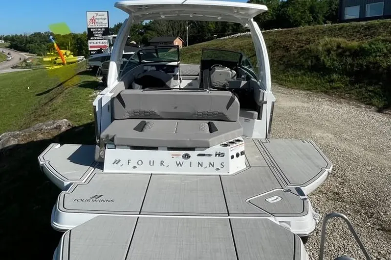 Slide: The Image of 2025 Four Winns H9 boat docked at marina, clear sky, and event tents in background. - 2