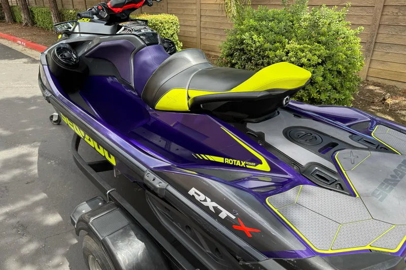 Slide: The Image of 2021 Sea-Doo RXT-X 300 jet ski, vibrant purple and yellow design, parked outdoors. - 2