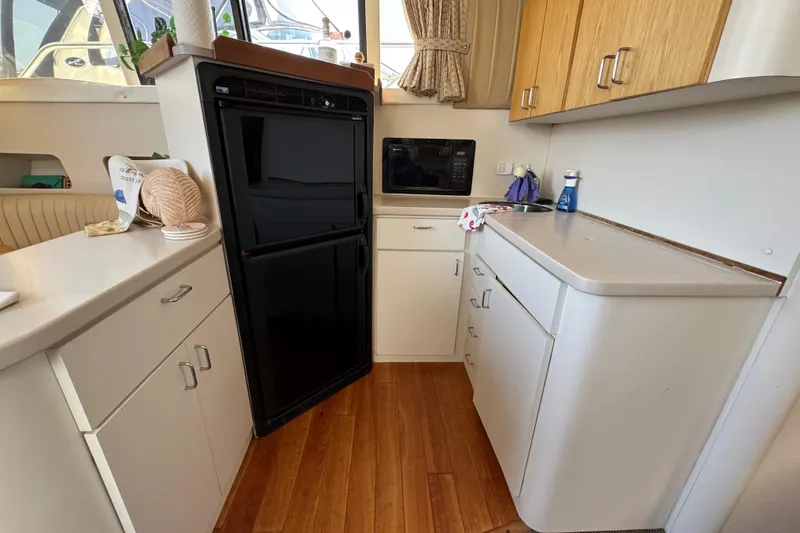 Slide: The Image of 1997 Mainship 40 Sedan Bridge kitchen with black fridge, microwave, and wooden cabinets. - 28