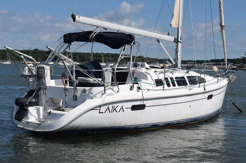 Slide: The Image of 2001 Hunter 340 sailboat named "Laika" docked on a calm lake under a blue sky. - 2