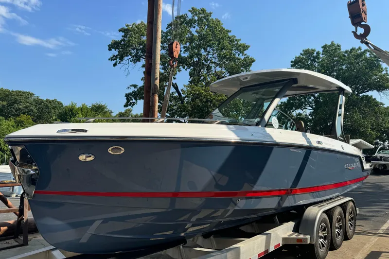 The Image of 2026 Monterey Elite 27 SD boat on trailer, blue hull, red stripe, sunny day, trees in background. - 1