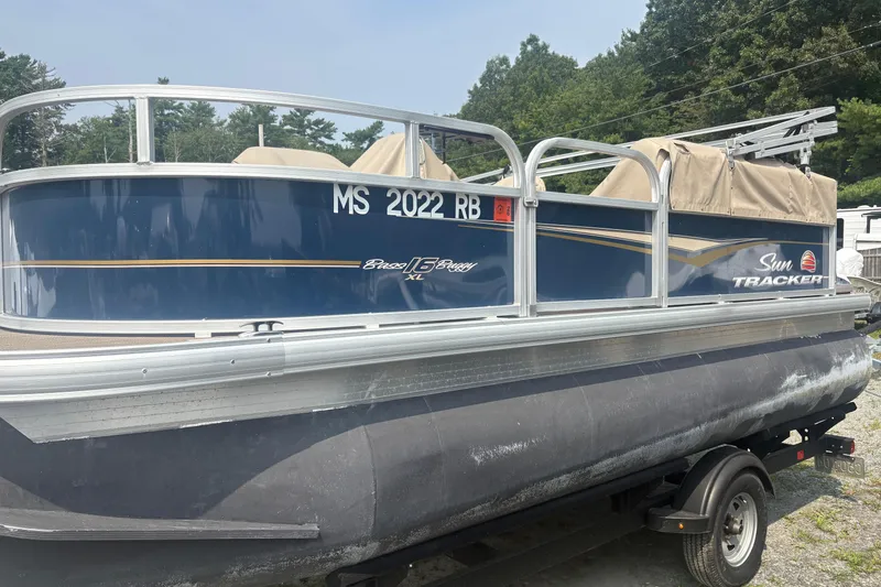 Slide: The Image of 2022 Sun Tracker Bass Buggy 16 XL pontoon boat on trailer, parked outdoors. - 2