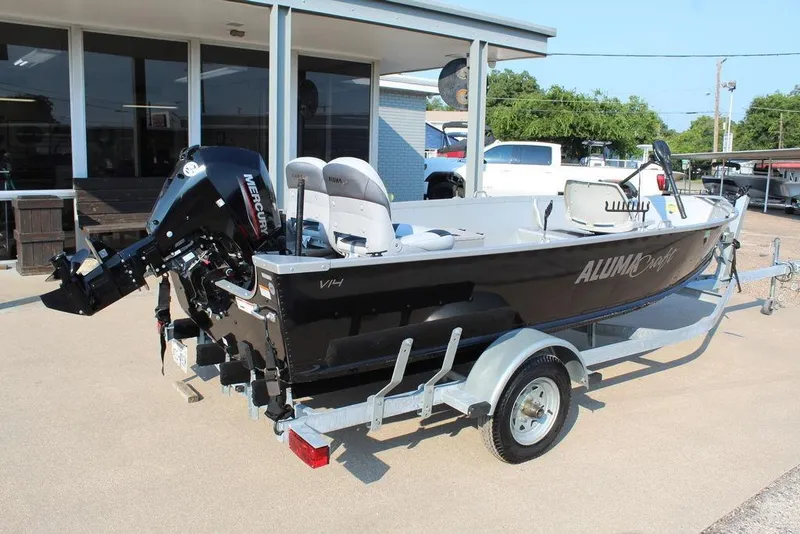 Slide: The Image of 2022 Alumacraft V14 boat on trailer with Mercury outboard motor, parked outside a building. - 2
