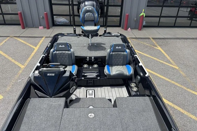 Slide: The Image of 2026 Bass Cat Puma STS boat interior with blue and gray seating, parked outside a garage. - 17