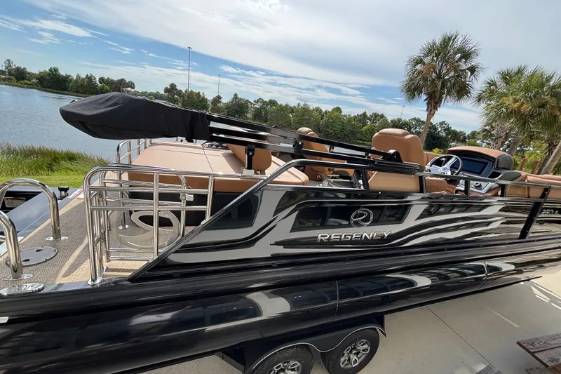Slide: The Image of 2025 Regency 250 LE3 Sport pontoon boat docked by a scenic lake. - 6