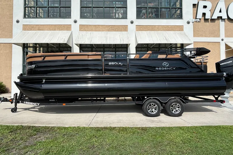 Slide: The Image of 2025 Regency 250 LE3 Sport pontoon boat on trailer, sleek black design, parked outdoors. - 2