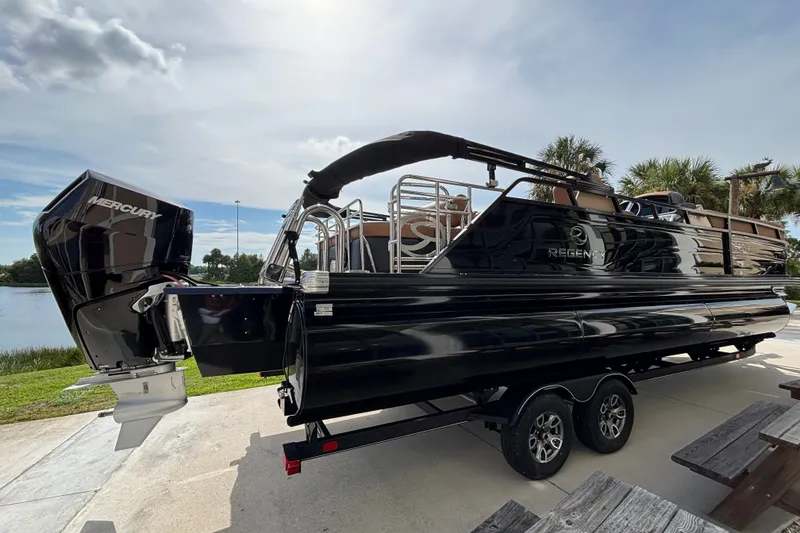 Slide: The Image of 2025 Regency 250 LE3 Sport pontoon boat with Mercury engine, parked near a lake. - 5