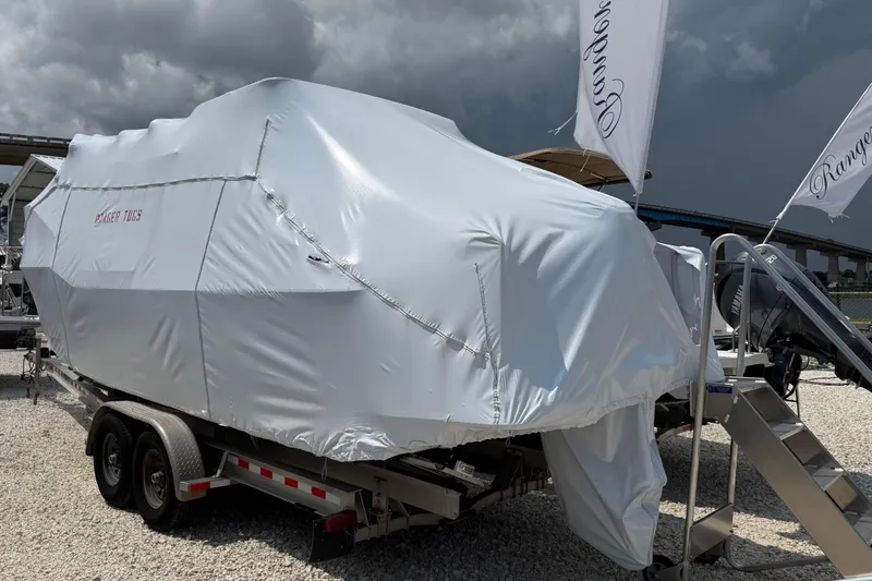 The Image of 2025 Ranger Tugs R-25 boat covered, displayed on a trailer under cloudy skies. - 1