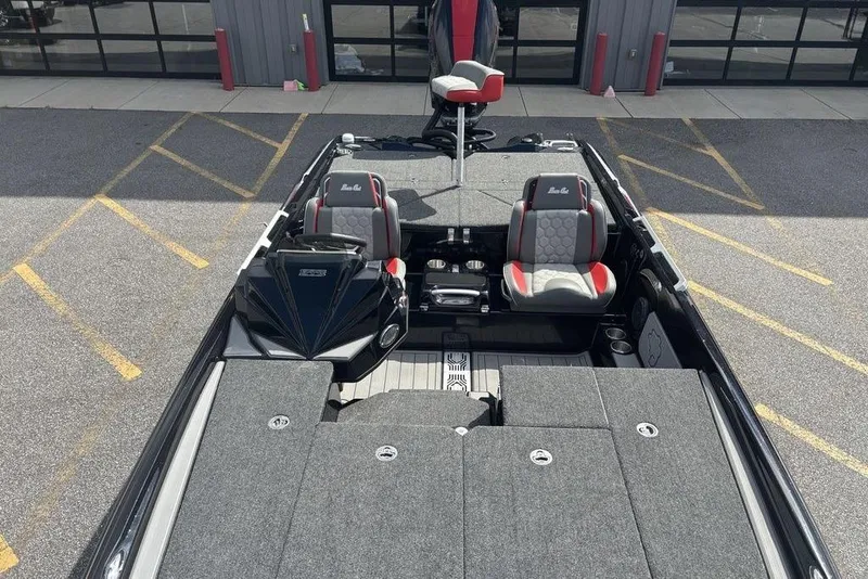 Slide: The Image of 2026 Bass Cat Jaguar STS boat interior with gray and red seating, parked outdoors. - 6