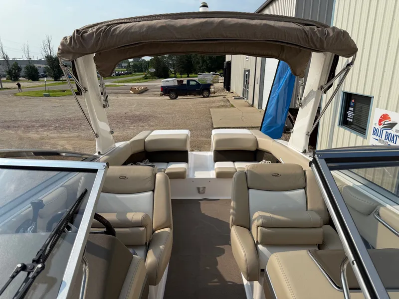 Slide: The Image of 2012 Regal 2700 Bowrider boat interior with beige seating and canopy, parked near a building. - 16