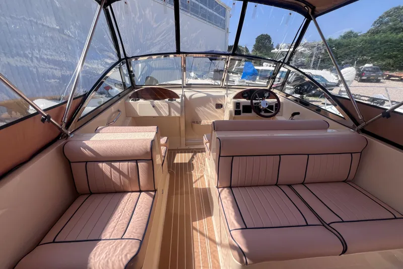 Slide: The Image of 2018 Rossiter 23 boat interior with beige seating and steering wheel, under clear canopy. - 16