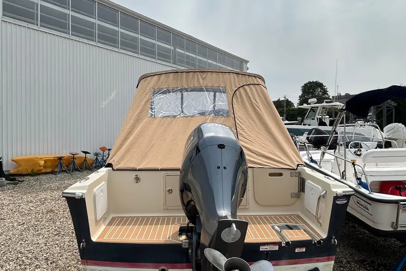 Slide: The Image of 2018 Rossiter 23 boat with tan cover and outboard motor in a marina. - 2