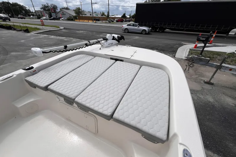 Slide: The Image of 2024 Carolina Skiff 21 LS boat with cushioned seating and trolling motor, parked near a road. - 13