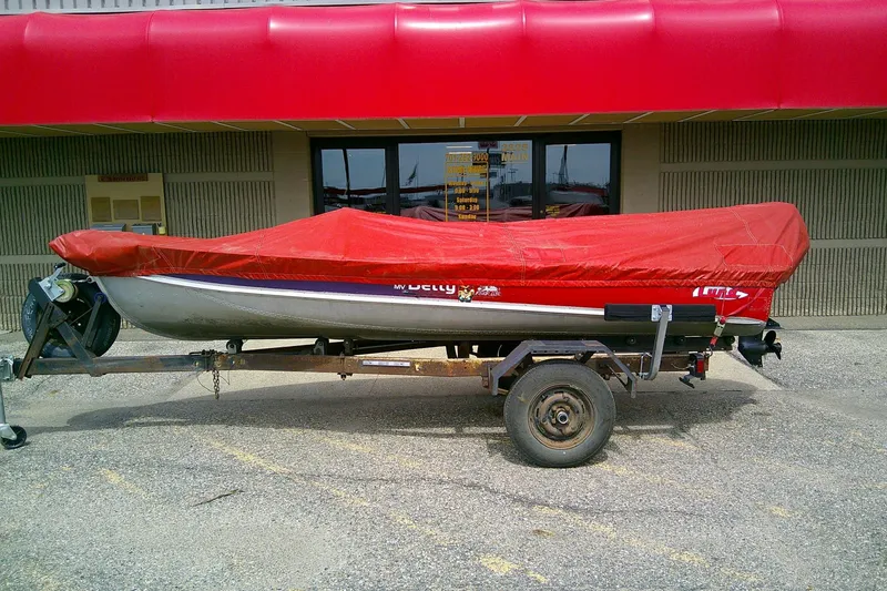 Slide: The Image of 1965 Lund V14 boat on trailer with red cover, parked outside a building. - 4