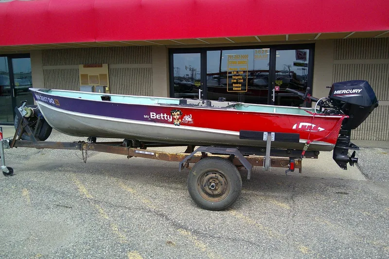 Slide: The Image of 1965 Lund V14 boat on trailer with Mercury outboard motor, parked outside a store. - 9