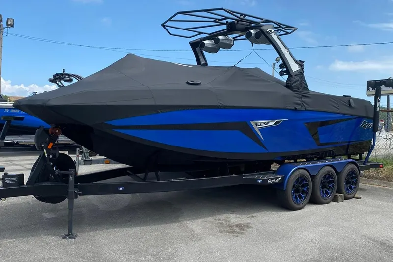 Slide: The Image of 2023 Tigé 24RZX boat with black cover on trailer, blue accents, parked outdoors. - 18