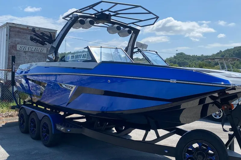 Slide: The Image of 2023 Tigé 24RZX boat in vibrant blue on a trailer, under a clear sky. - 2