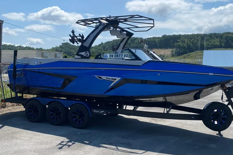 Slide: The Image of 2023 Tigé 24RZX boat in vibrant blue on a trailer, under a sunny sky. - 3