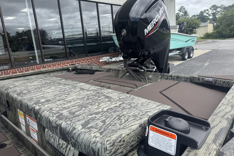 Slide: The Image of 2026 Tracker Grizzly 1860 CC boat with Mercury engine, camo design, parked outside. - 6