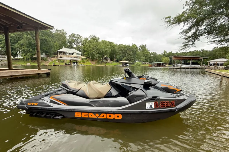 Slide: The Image of 2021 Sea-Doo GTX 230 jet ski on a calm lake near docks and trees. - 2