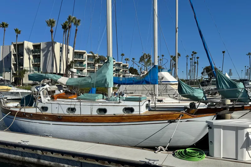 The Image of Vintage 1978 Baba Cutter sailboat docked in marina with palm trees and buildings in background. - 0