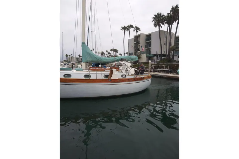 Slide: The Image of 1978 Baba Cutter sailboat docked in marina, surrounded by palm trees and buildings. - 10