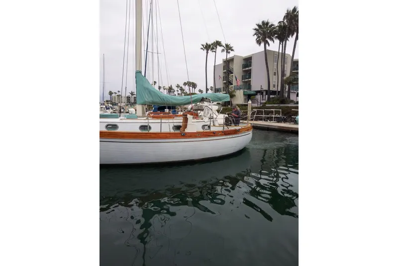 Slide: The Image of Vintage 1978 Baba Cutter sailboat docked in marina, surrounded by palm trees and buildings. - 14