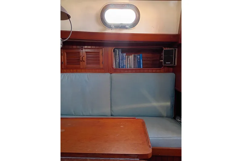 Slide: The Image of Interior of a 1978 Baba Cutter sailboat with wooden cabinetry and blue cushions. - 16