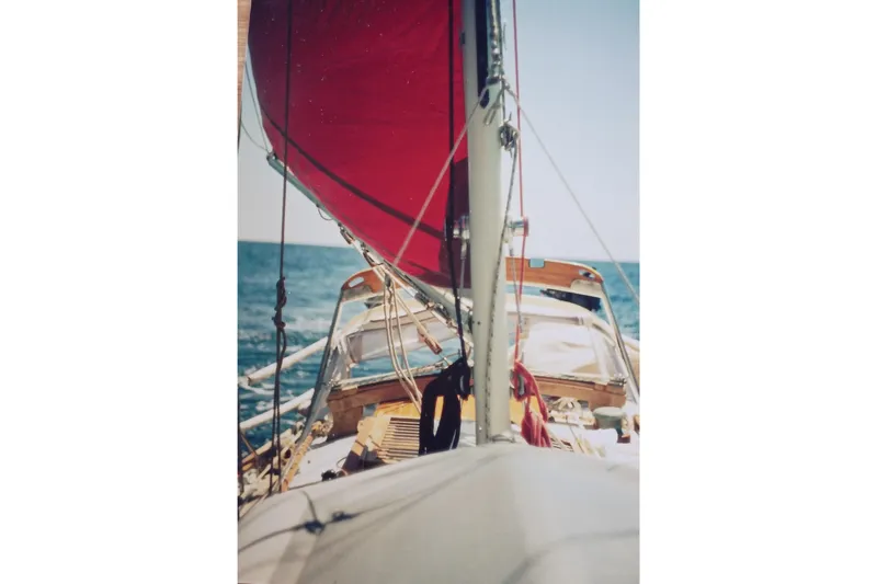 Slide: The Image of Sailing on a 1978 Baba Cutter with red sails over blue ocean waters. - 2