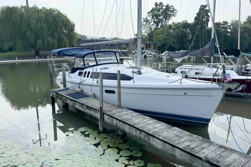 The Image of 1995 Hunter 336 sailboat docked on a calm lake with lush greenery. - 0