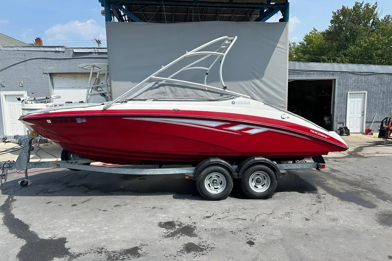 Slide: The Image of 2015 Yamaha AR210 boat in red on a trailer, parked outdoors. - 0