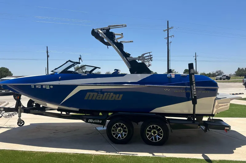 Slide: The Image of 2021 Malibu Wakesetter 21 MLX boat on trailer, blue and white design, parked outdoors. - 6