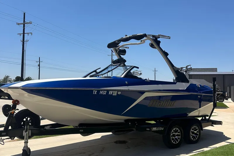 Slide: The Image of 2021 Malibu Wakesetter 21 MLX boat on trailer, blue and white design, sunny day. - 7