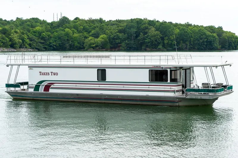 Slide: The Image of 1995 Lakeview 62 x 14 Widebody Houseboat on serene lake with lush green backdrop. - 1