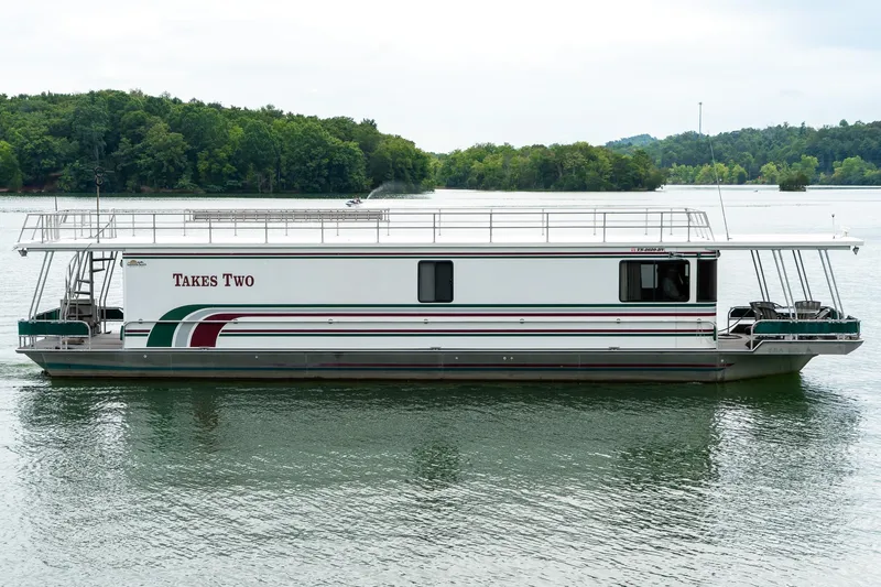 Slide: The Image of 1995 Lakeview 62 x 14 Widebody Houseboat on serene lake with lush green backdrop. - 2