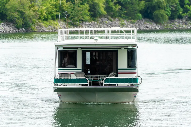Slide: The Image of 1995 Lakeview 62 x 14 Widebody Houseboat cruising on a serene lake with lush greenery. - 8