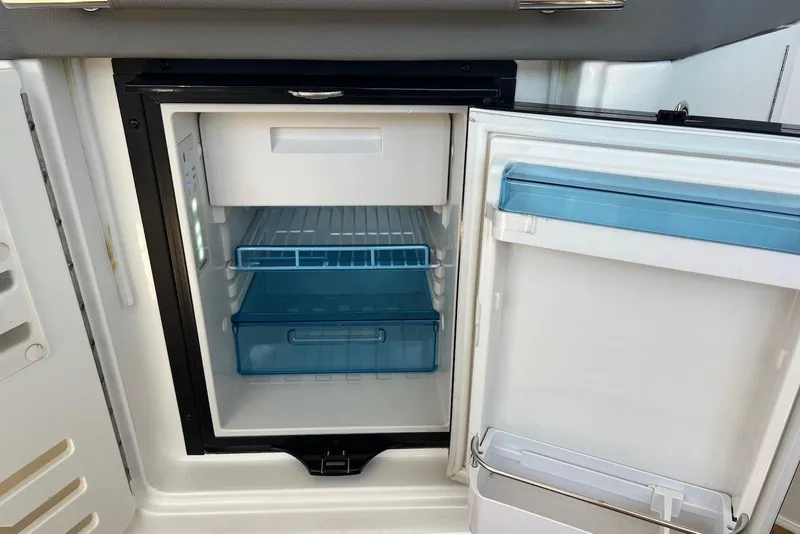 Slide: The Image of Open refrigerator inside 2022 Sea Ray SLX 310 Outboard boat, featuring blue storage drawers. - 33