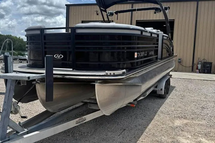 Slide: The Image of 2020 Harris Solstice 250 pontoon boat on trailer, parked outside a building. - 1