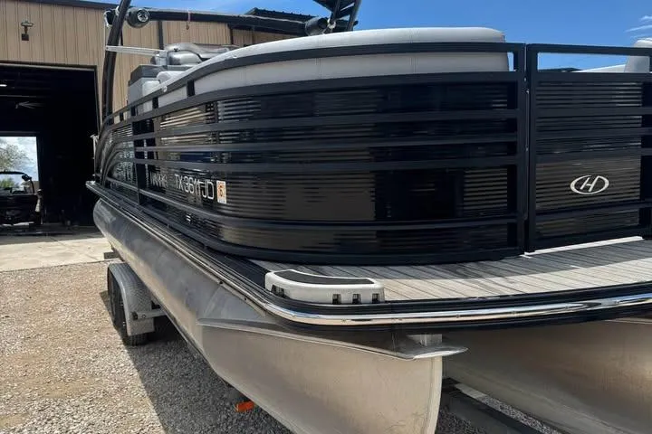 Slide: The Image of 2020 Harris Solstice 250 pontoon boat parked outside a garage on a sunny day. - 12